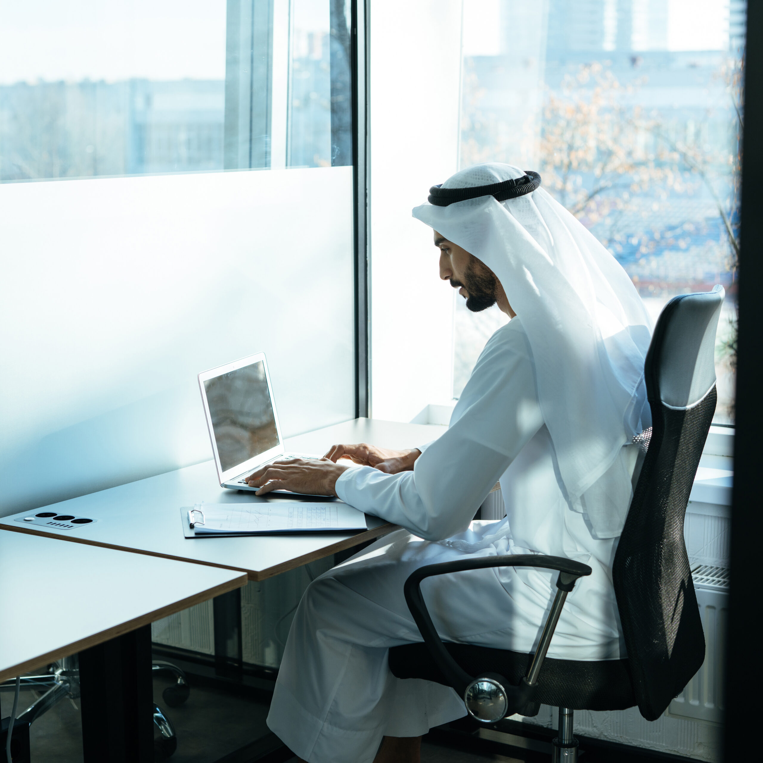 handsome man with dish dasha working in his business office of Dubai. Portraits of a successful businessman in traditional emirates white dress. Concept about middle eastern cultures, lifestyle and professional occupations